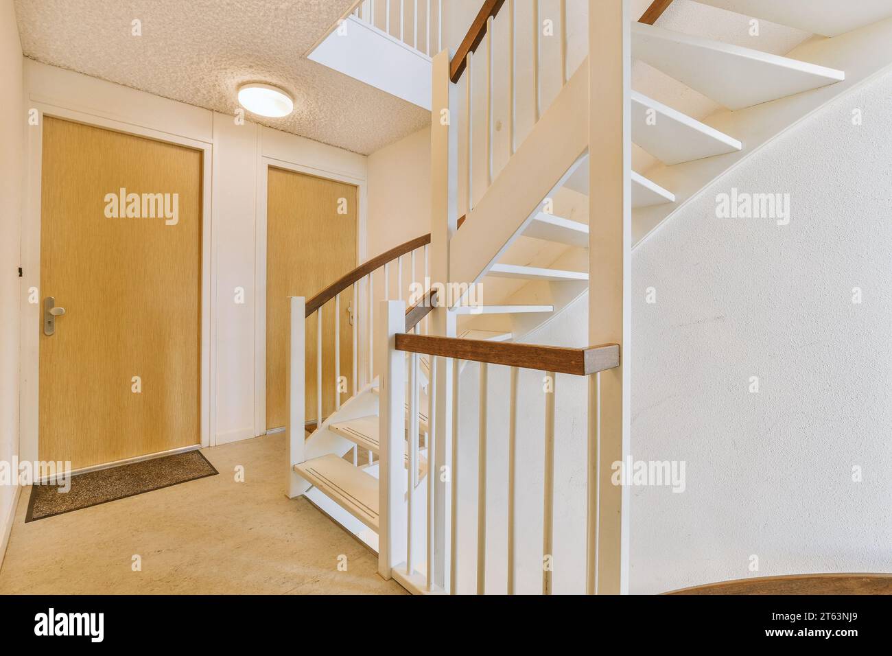 Flur mit Holztüren verschiedener Zimmer und Wendeltreppe, die in die obere Etage des modernen weißen Hauses führt Stockfoto