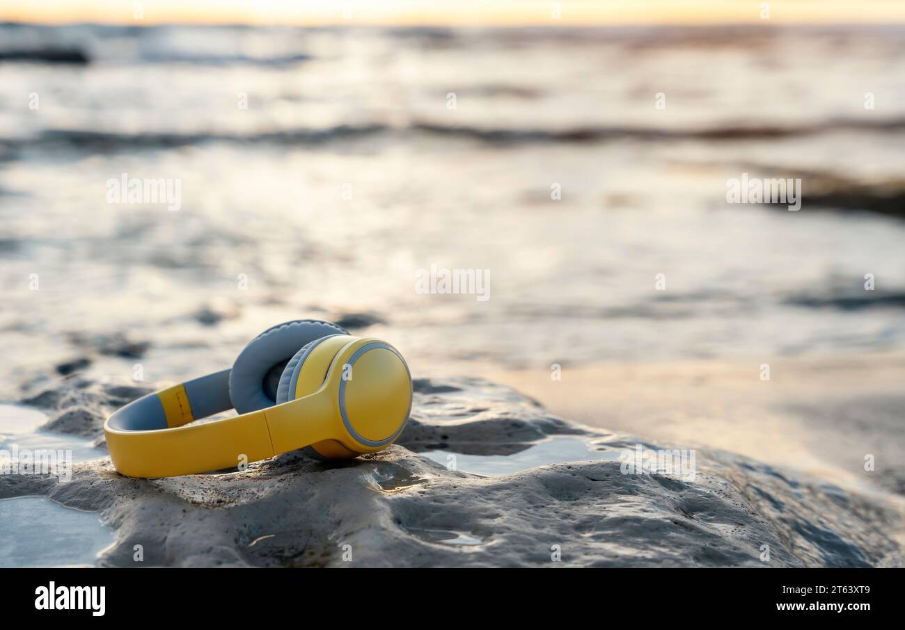 Kopfhörer am Strand auf dem Sand in der Nähe des Meeres bei Sonnenuntergang. Nehmen Sie Musik oder Buch mit auf eine Reise, hören Sie die Musik der Natur. Kopierbereich Stockfoto