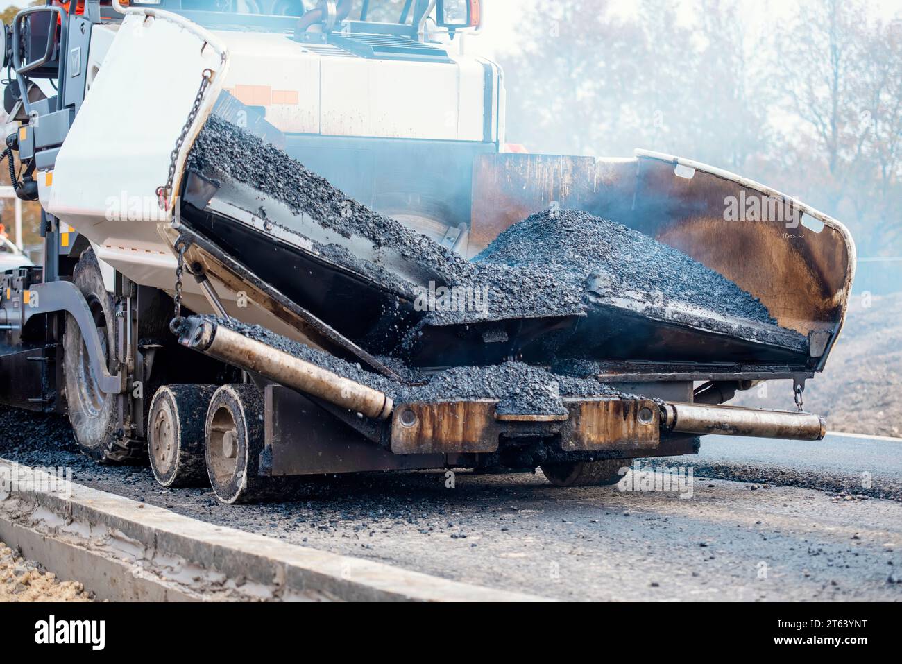 Asphaltfertiger mit heißem Asphalt, der neue Straßenoberflächen auf neuen Wohnbaustellen verlegt, und Straßenarbeiter in orangefarbenem Hi-viz als nächstes Stockfoto