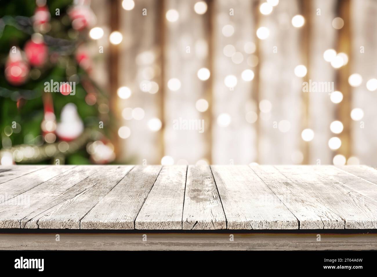 Ein sauberer, weißer Holztisch zur Produktpräsentation mit zauberhaften Weihnachtsbaumlichtern in Bokeh. Ideale Einrichtung für ein fesselndes und fes Stockfoto