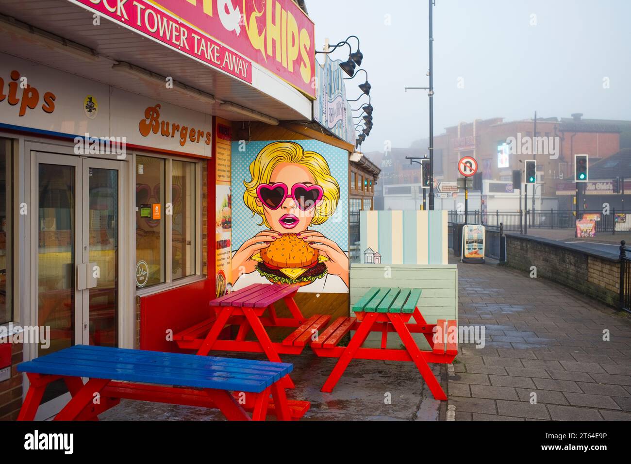 Grafische Bilder einer Frau, die einen Burger vor einem Skegness Restaurant und zum Mitnehmen isst Stockfoto