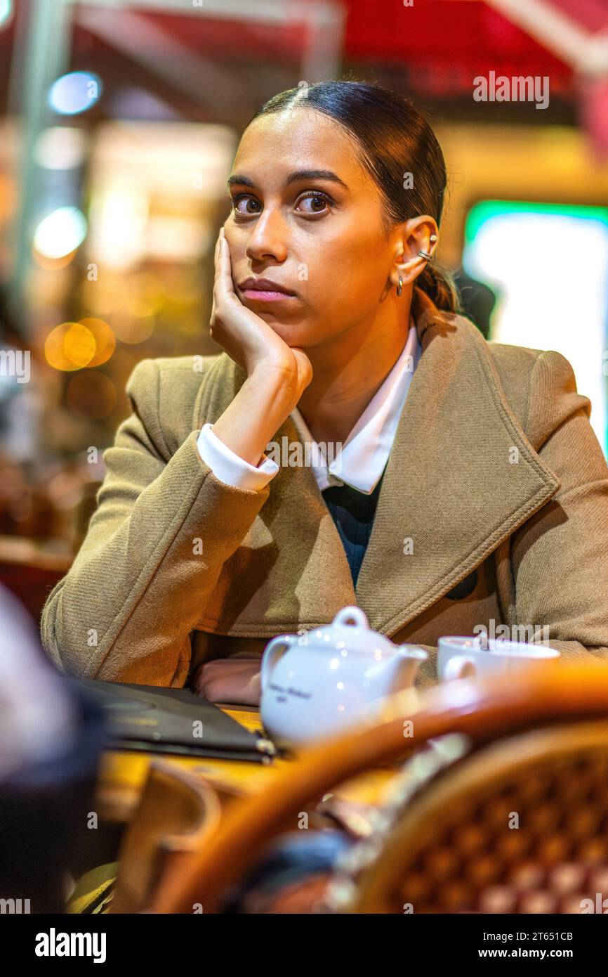 Eine junge Frau, die mit viel Aufmerksamkeit anstarrt und sich Kopf auf Hand an den Kaffeetisch mit Tee ausruht - Paris, Frankreich. Stockfoto
