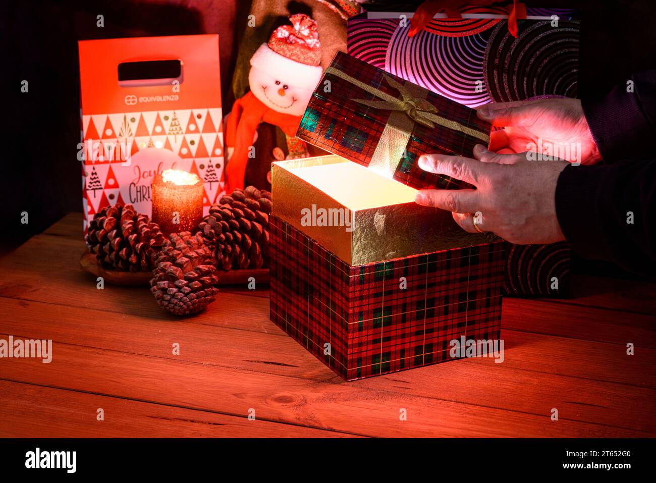 Details zu den Händen, die eine Weihnachtsgeschenkbox öffnen, von der aus ein helles Licht leuchtet. Weihnachtsstillleben mit dunklem Hintergrund, beleuchtet durch Dose Stockfoto