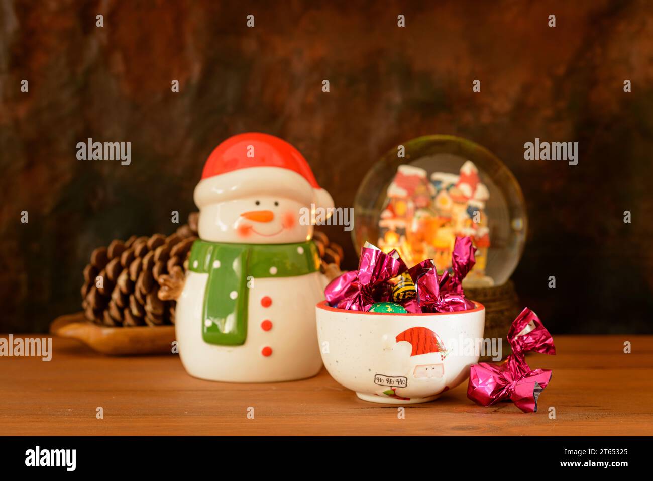 Weihnachtsstillleben mit Porzellanfiguren und anderen Gegenständen, Süßigkeiten und Pralinen, auf einem Holztisch mit dunklem Hintergrund. Stockfoto
