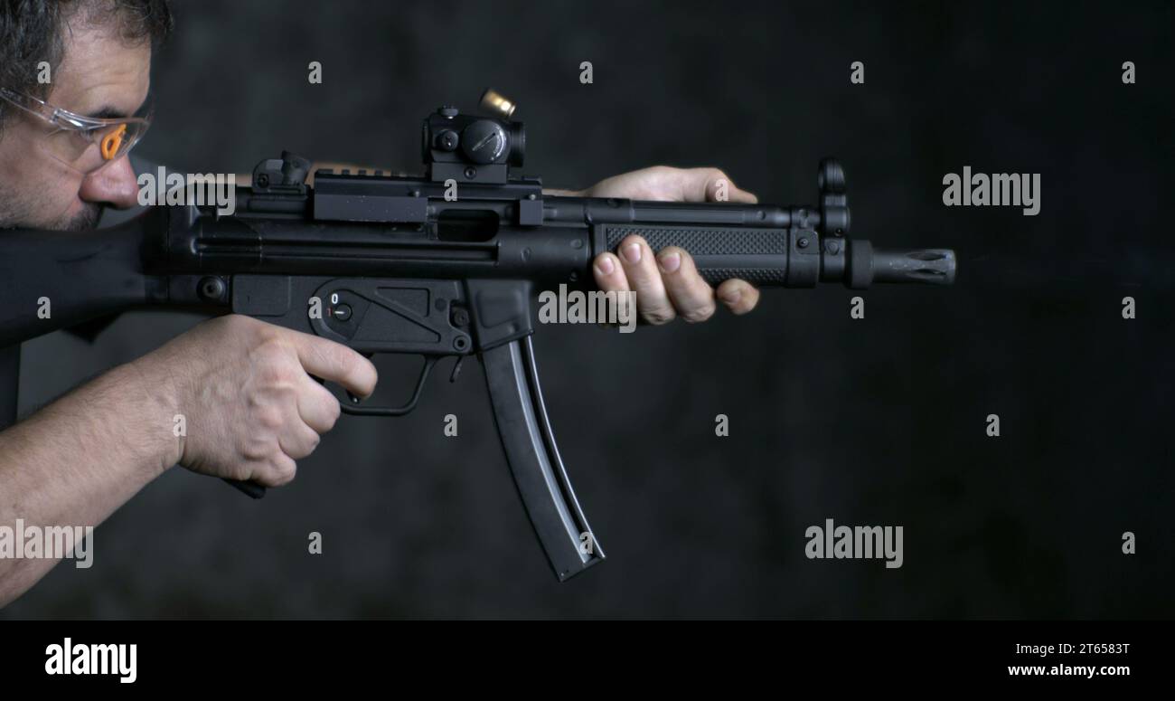 Feuernde Waffe in Hochgeschwindigkeitsgeschwindigkeit, HK SP5K-KANONE, Seitenansicht. Person, die auf deutsches Sturmgewehr zielt und schießt Stockfoto