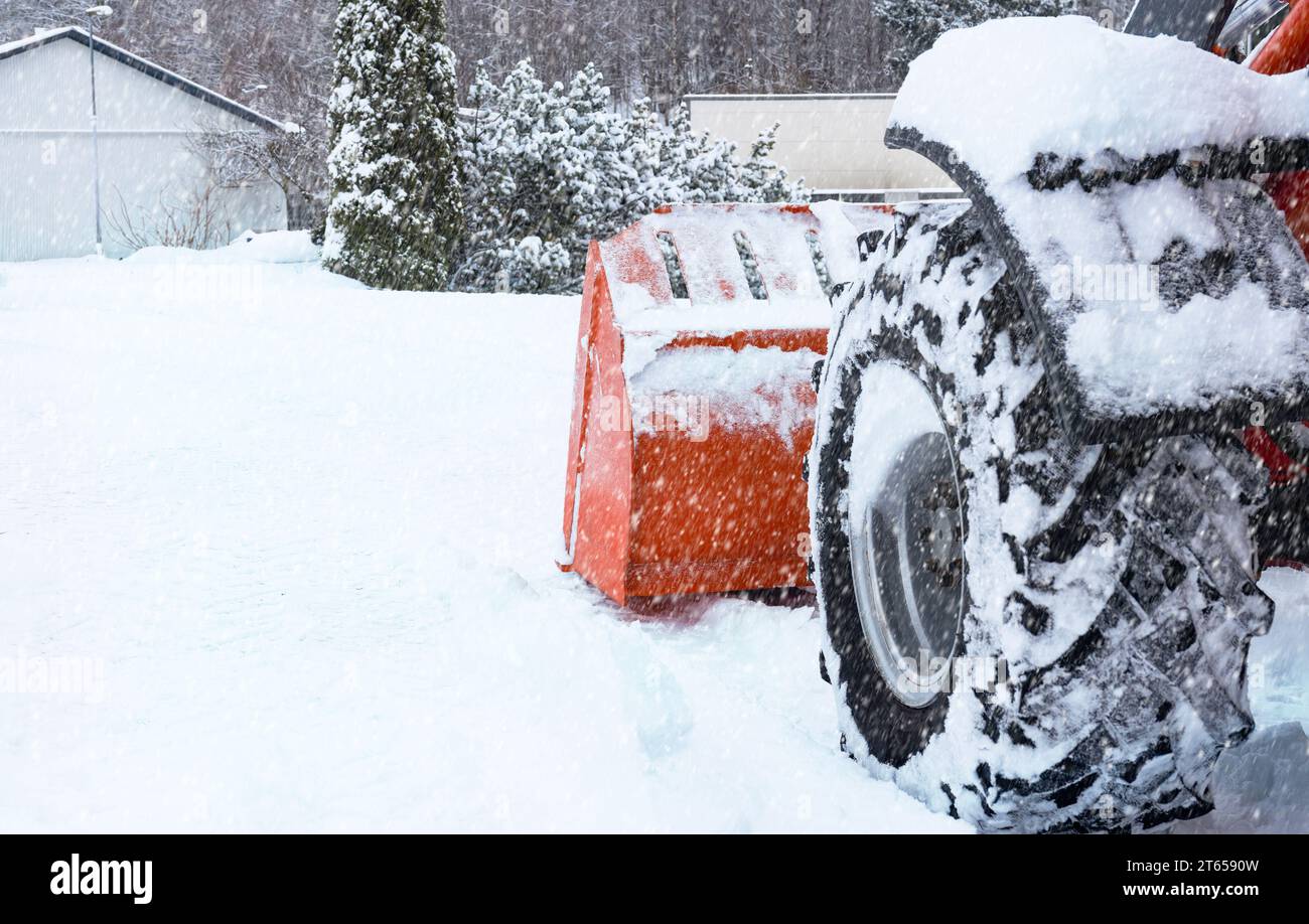 Roter Traktor mit Schneepflug entfernt Schnee bei Schneefall. Wetterbedingungen im Blizzard. Straßenpflege im Winter. Ziehen Sie sich auf Stockfoto