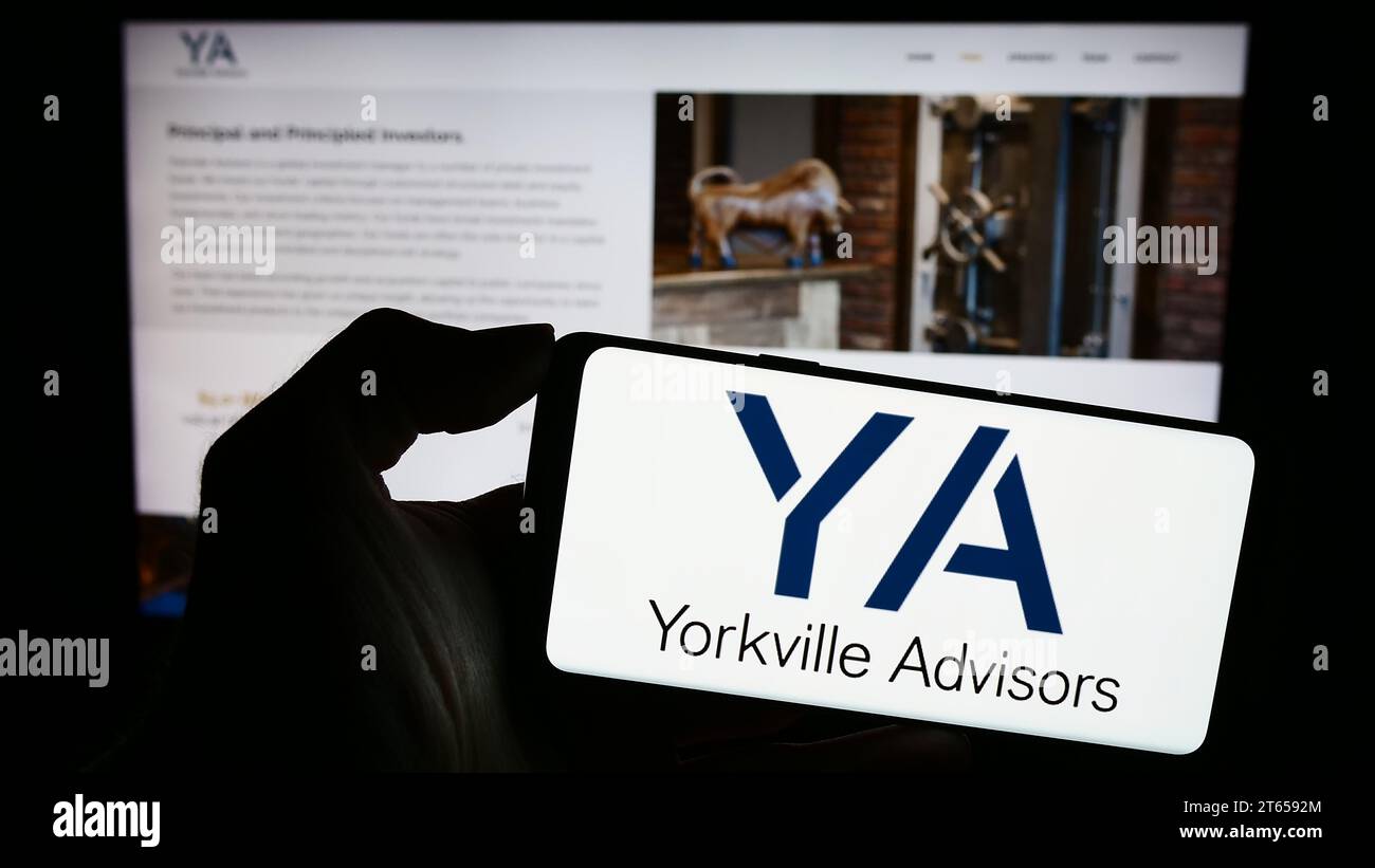 Person mit Mobiltelefon und Logo der amerikanischen Investmentgesellschaft Yorkville Advisors Global LP vor der Webseite. Schwerpunkt auf dem Display des Telefons. Stockfoto