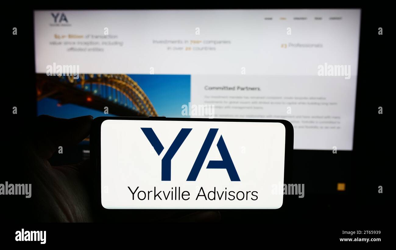 Person, die ein Mobiltelefon mit dem Logo der US-amerikanischen Investmentgesellschaft Yorkville Advisors Global LP vor der Website des Unternehmens hält. Schwerpunkt auf dem Display des Telefons. Stockfoto
