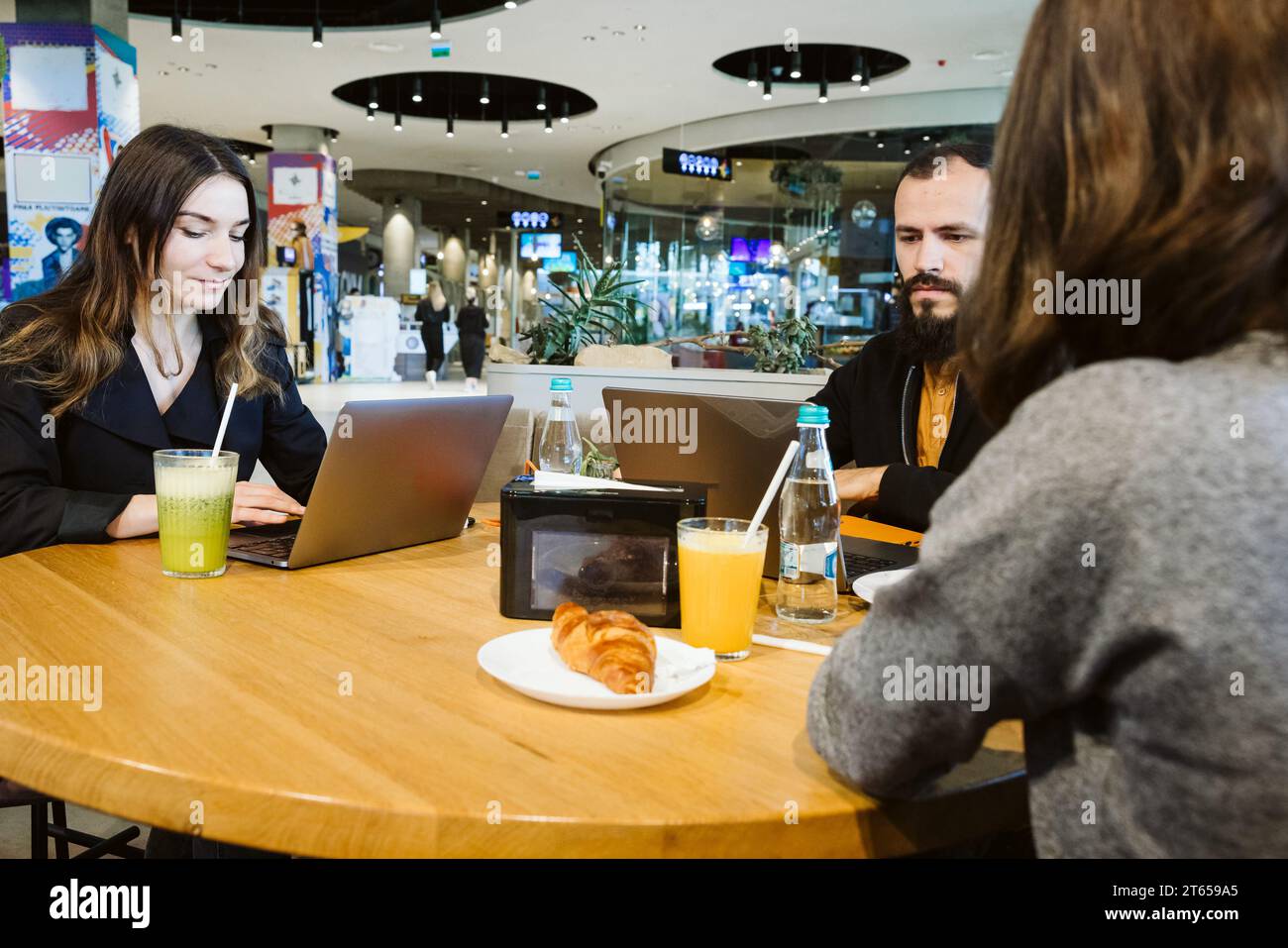 Zwei Frauen und ein Mann mit einem Kind arbeiten von ihren Laptops in einem Einkaufszentrum Stockfoto