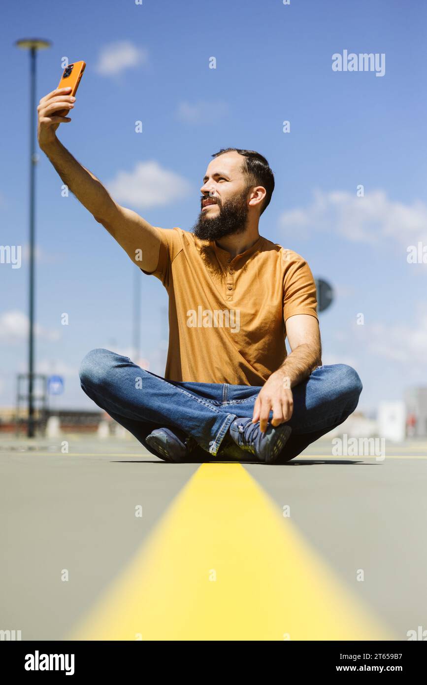 Junger Mann in Lotus-Position, der auf der Straße einen Videoanruf macht Stockfoto