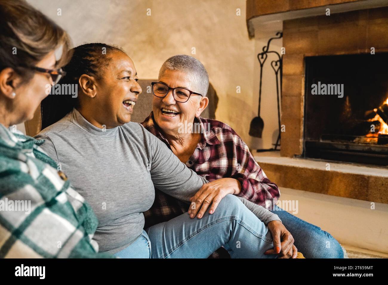 Multirassische Seniorenfreunde am Holzkamin, die gemeinsam Spaß im ländlichen Haus haben. Winter- und Herbstsaison mit Life-Style-Konzept Stockfoto