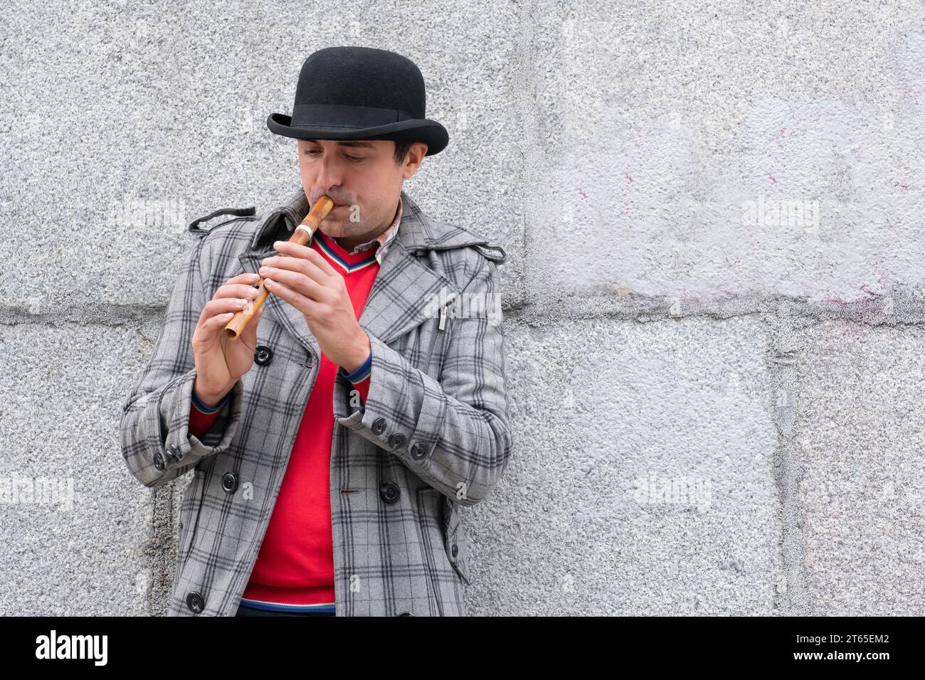 Ein Mann spielt ein Sopilka-Musikinstrument auf der Straße vor dem Hintergrund der Mauer Stockfoto