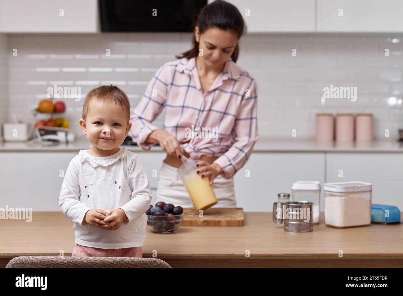 Glückliche kleine Tochter mit ihrer Mutter, die in der Küche kocht. Zusammen backen Stockfoto