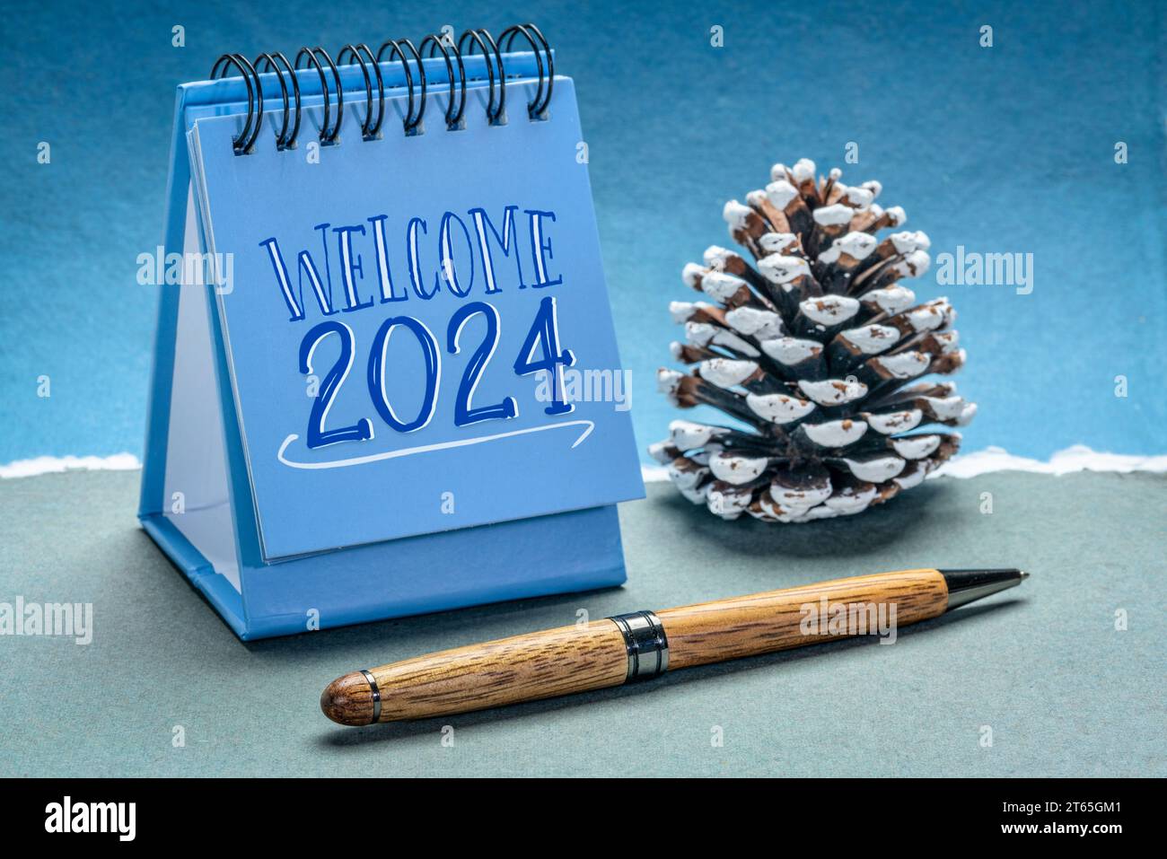 Begrüßen Sie 2024 in einem spiralförmigen Tischkalender mit dekorativem, frostigem Kiefernzapfen auf handgemachtem Papier, Neujahrskonzept Stockfoto