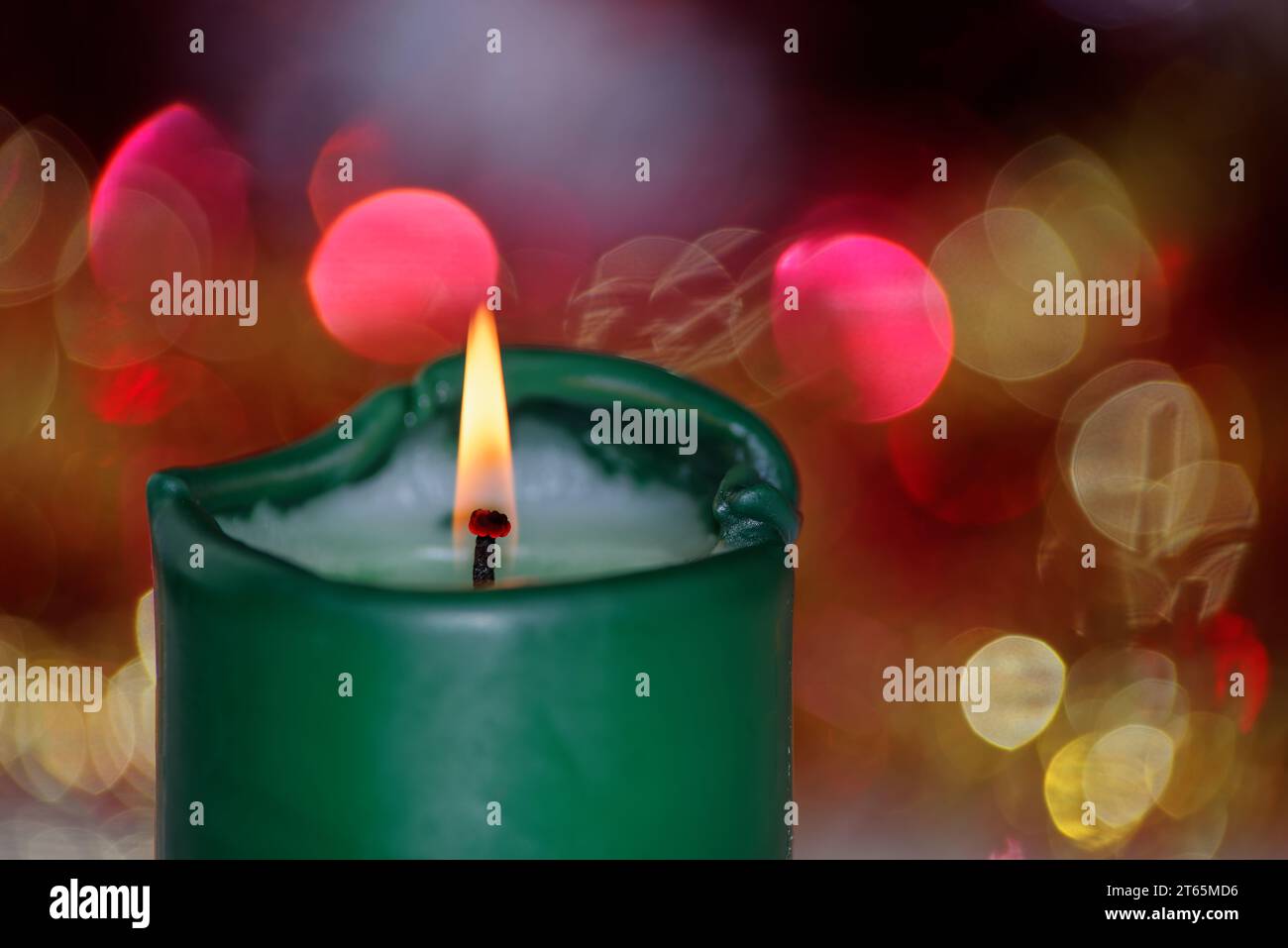 Grüne brennende Kerze vor bunt verschwommenem Hintergrund. Konzentrieren Sie sich auf die Flamme Stockfoto