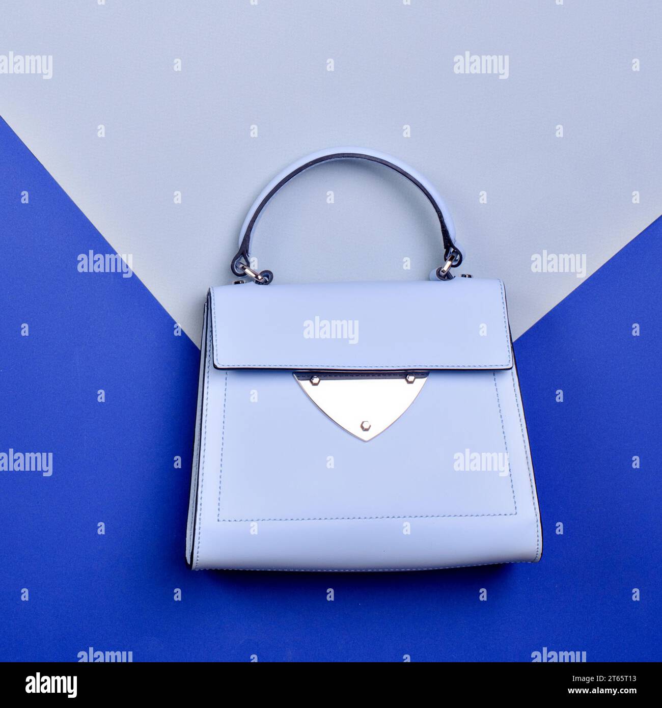 Moderne Umschlagtasche für Frauen mit Obergriff aus hellblauem Leder mit silbernen Metallbeschlägen auf einem kreativen grafischen Hintergrund. Kreatives Modell für Werbung Stockfoto