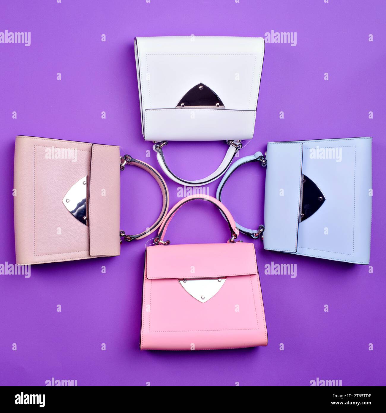 Vier schicke Damengeldbörsen mit Patte im gleichen Design, aber in verschiedenen Farben auf lila Hintergrund. Auswahl des Zubehörs durch einen Stylisten. C Stockfoto