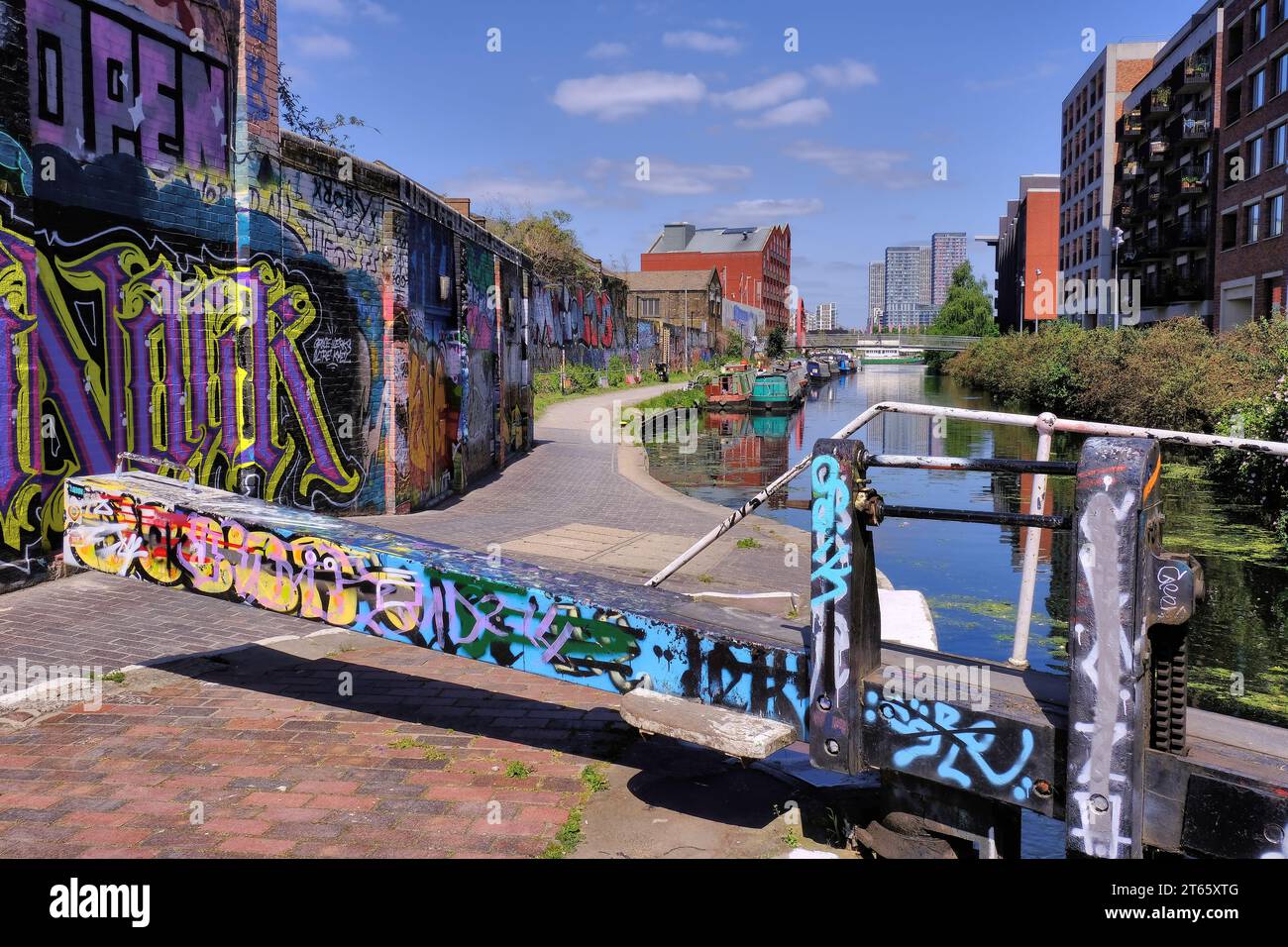 Kingsland: Schleusentore und farbenfrohe Street Art (Graffiti) am Hertford Union Canal mit Booten, Reflexionen und Blick auf Stratford, London, England, Großbritannien Stockfoto