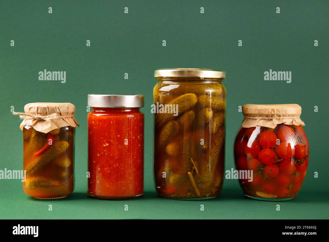 Gemüse in Dosen in geschlossenen Glasgläsern auf grünem Hintergrund. Eingelegte Gurken, Tomaten, Chili-Sauce, Adjika. Scharfer Snack, Hausmannskost. Stockfoto