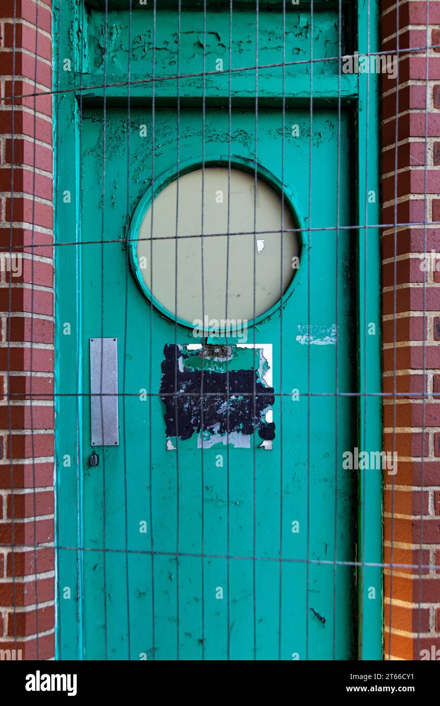 Baufällige alte grüne Tür, die durch Drahtzäune geschützt und blockiert ist. Stockfoto