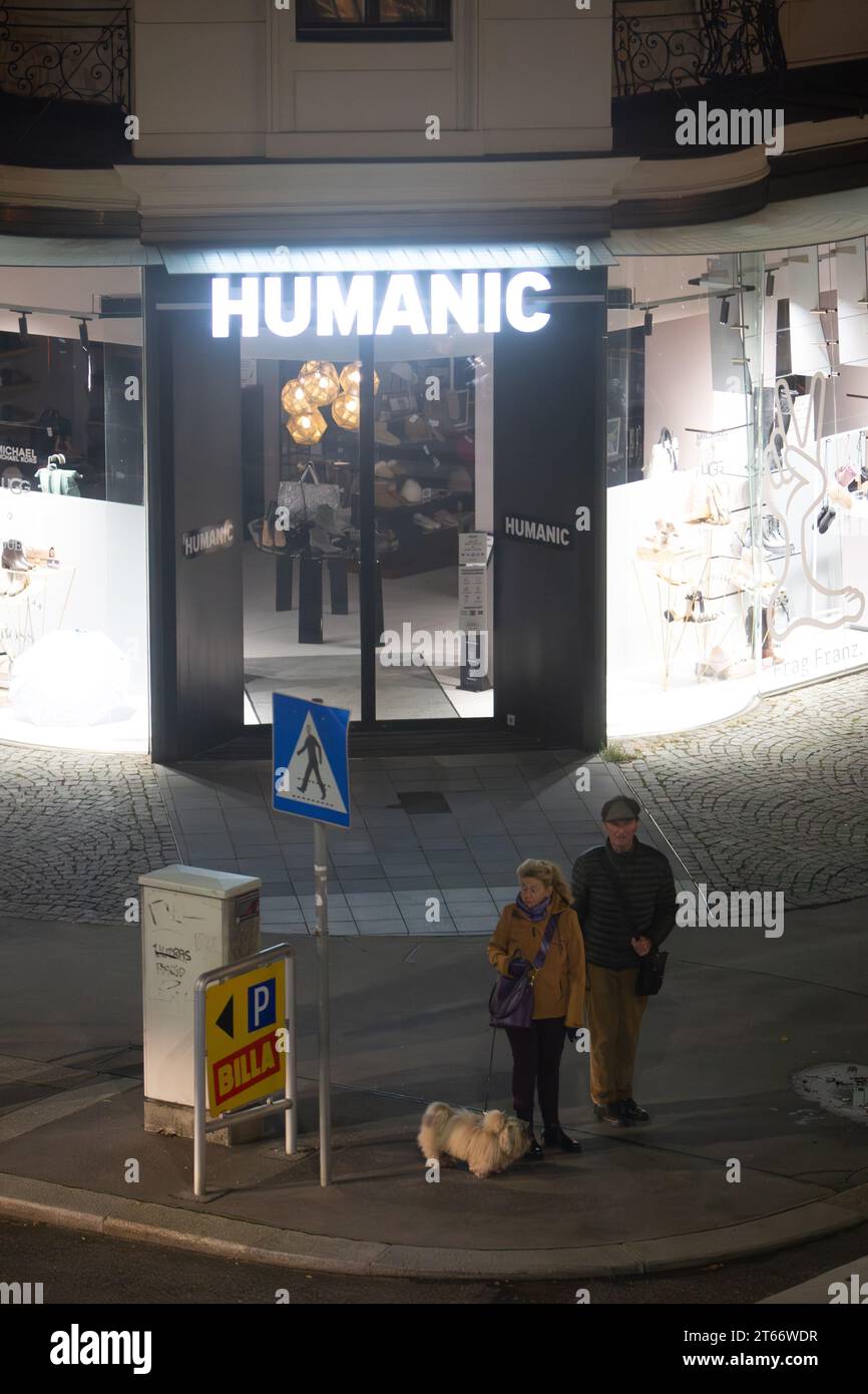Ein paar Männer und Frauen und ihr Hund spazieren nachts im Winter vor dem Humanic Store in Wien Österreich, fotografiert von einem hohen Gebäude Stockfoto