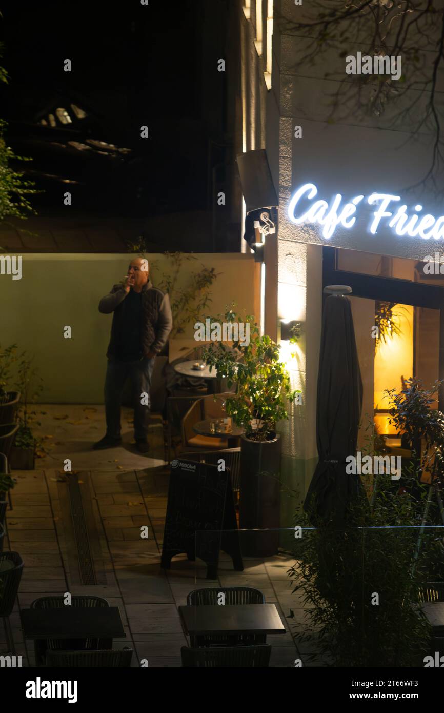 Ein kahler Mann raucht, während er an einem Winterabend beiläufig vor einem Café steht, Wien Österreich, Stockfoto
