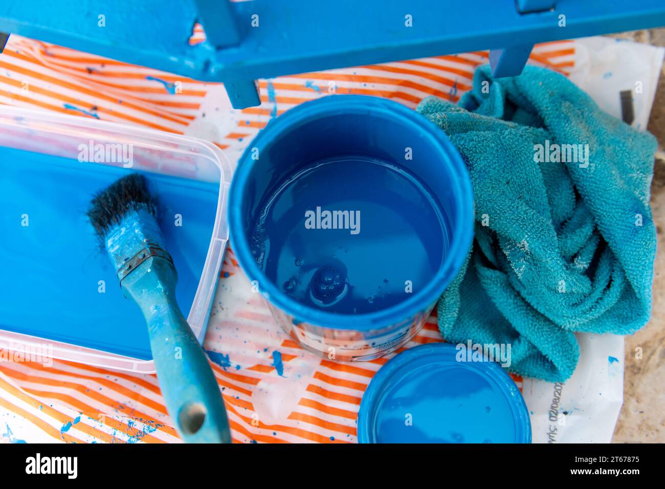 Einen Metallzaun mit einer Dose blauer Farbe und Pinsel streichen. Verbesserungen im Haushalt. Stockfoto
