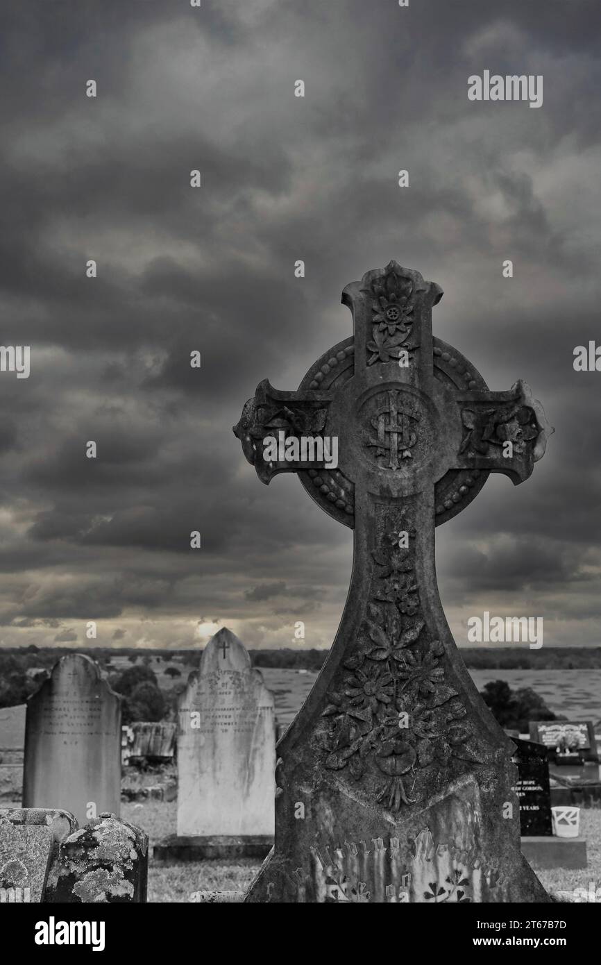Schwarz-weißer Grabstein des keltischen Kreuzes eines christlichen Grabes in einem Friedhof mit stürmischem Himmel. Stockfoto