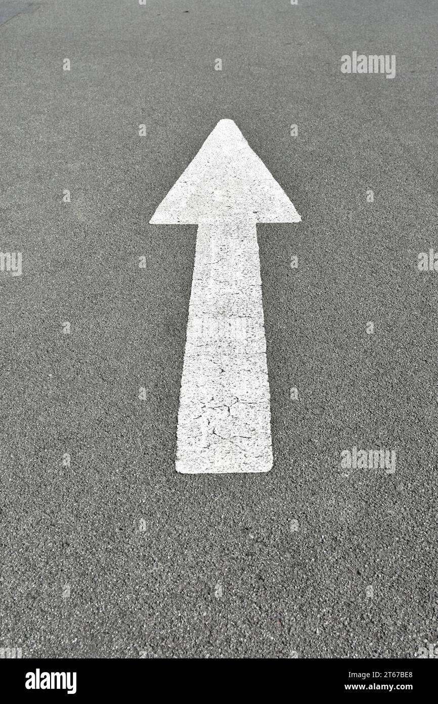 Weiß lackiertes Pfeil- oder Straßenmarkierungsschild, das den Weg nach vorn zeigt. Stockfoto