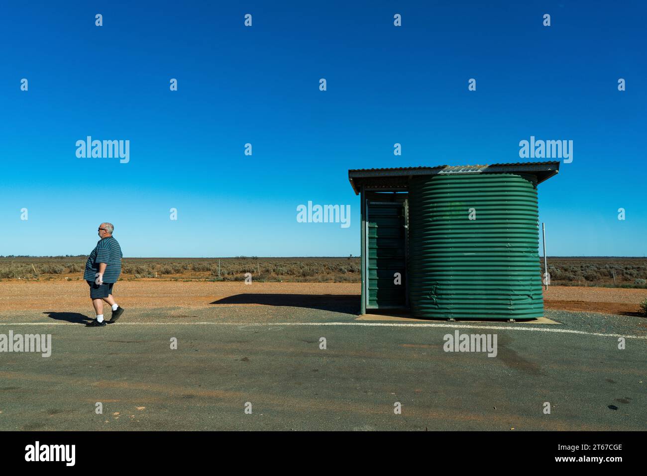 Ein großer Mann läuft in der Nähe einer Toilette am Straßenrand auf dem Silver City Highway in der Nähe von Broken Hill NSW. Stockfoto