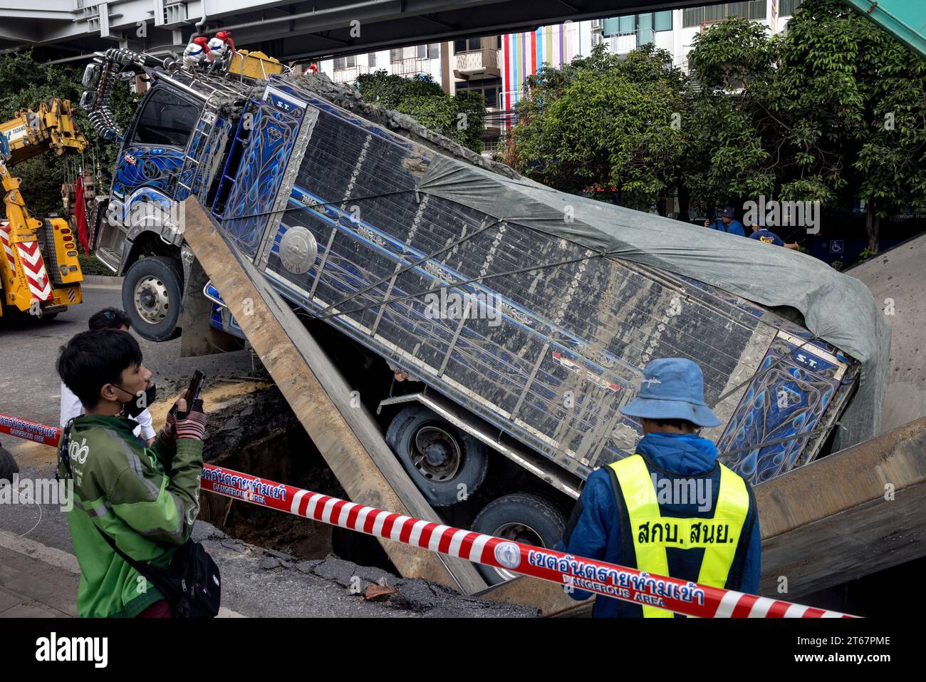 Ein LKW sitzt in einem Abschnitt der eingestürzten Straße, nachdem der Boden unter dem Gewicht des vorbeifahrenden Fahrzeugs am 8. November 2023 auf der Sukwhumwit Road in Bangkok, Thailand, nachgegeben wurde. Zwei Menschen wurden nach dem Vorfall, der sich heute Morgen auf Bangkoks belebtester Straße ereignete, ins Krankenhaus gebracht. Der LKW transportierte Schmutz und Schlamm von einer Baustelle, als die Stahlplatten, die zur Abdeckung eines Tunnels verwendet wurden, nach innen fielen. Der Unfall hat während der Mittagszeit zu Staus von mehreren Kilometern geführt. Die Zuschauer beschrieben einen lauten Knall, bevor der Lkw durch den Boden stürzte. Zwei Motorräder Stockfoto