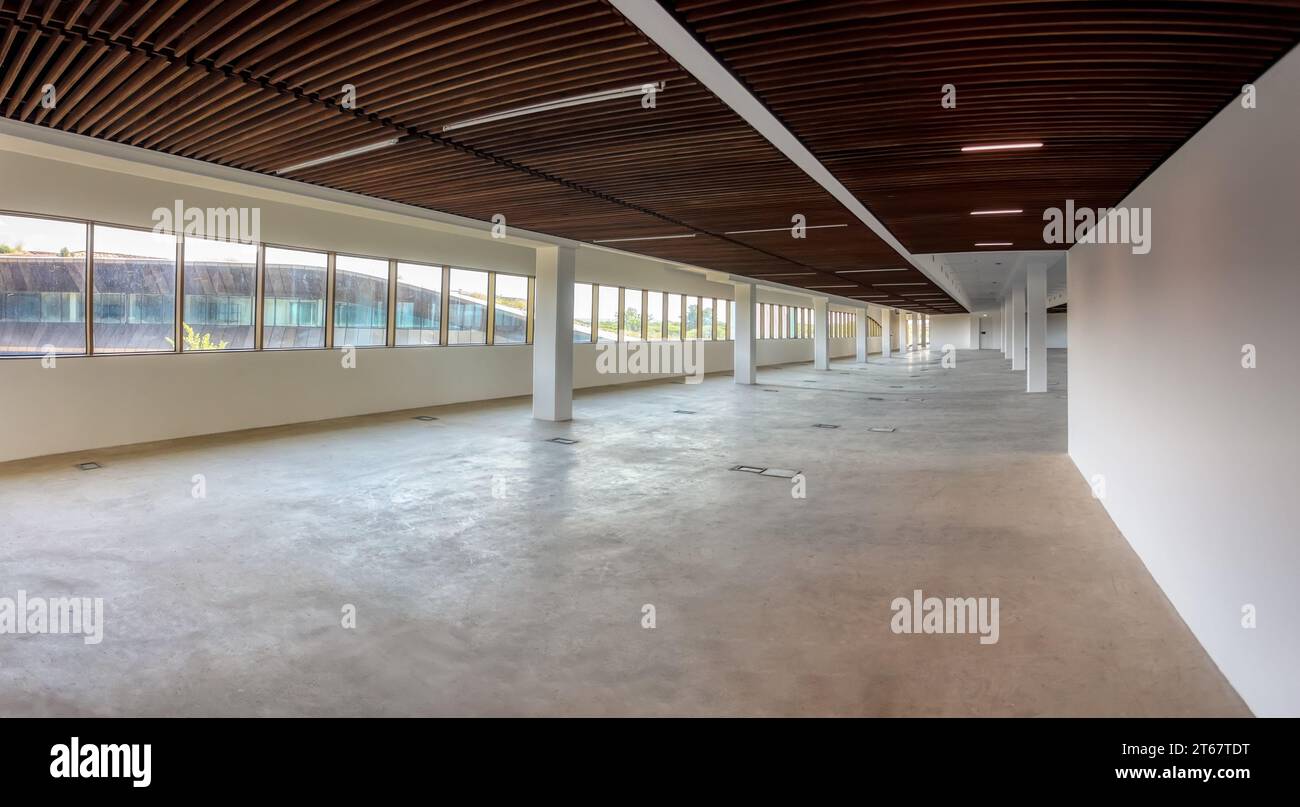 Leeres langes Geschäftsgebäude mit Fensterbeleuchtung, Innenbereich, Zementboden und weißen Wänden, schwindende Perspektive. Stockfoto