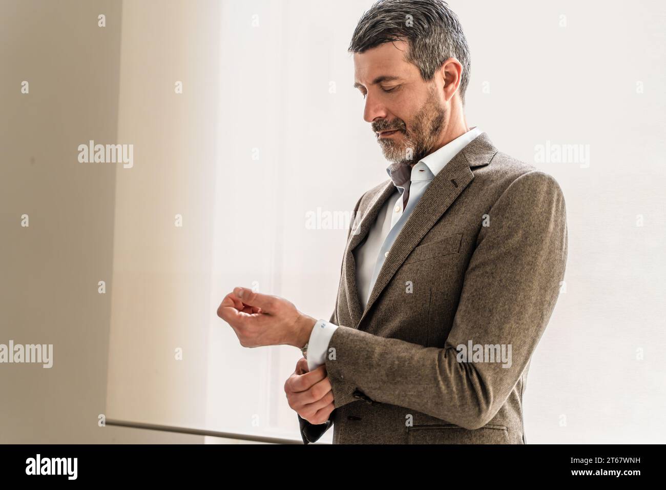 Ein reifer Geschäftsmann passt seine Hemdmanschette sorgfältig an und betont die Aufmerksamkeit auf das professionelle Erscheinungsbild. Stockfoto