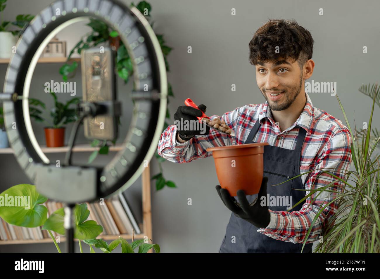 Arabische männliche Gärtner Influencer Filme Video für Blog gibt Empfehlungen, wie man Topfblume transplantiert, Gießen Drainage sendet Livestream Stockfoto