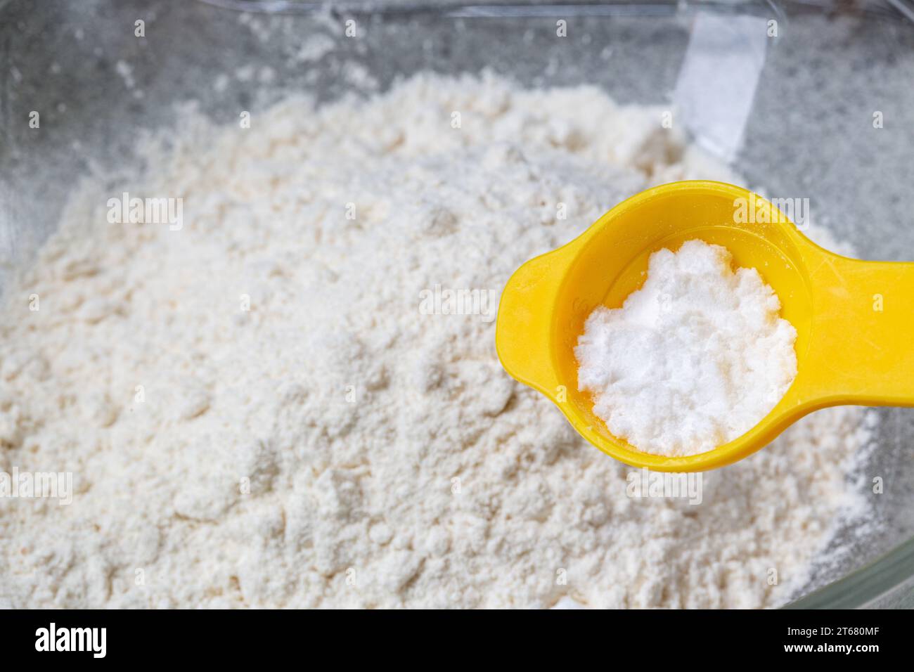 Ein gelber Teelöffel mit Tatarcreme über einer Schüssel weißem Mehl. Stockfoto