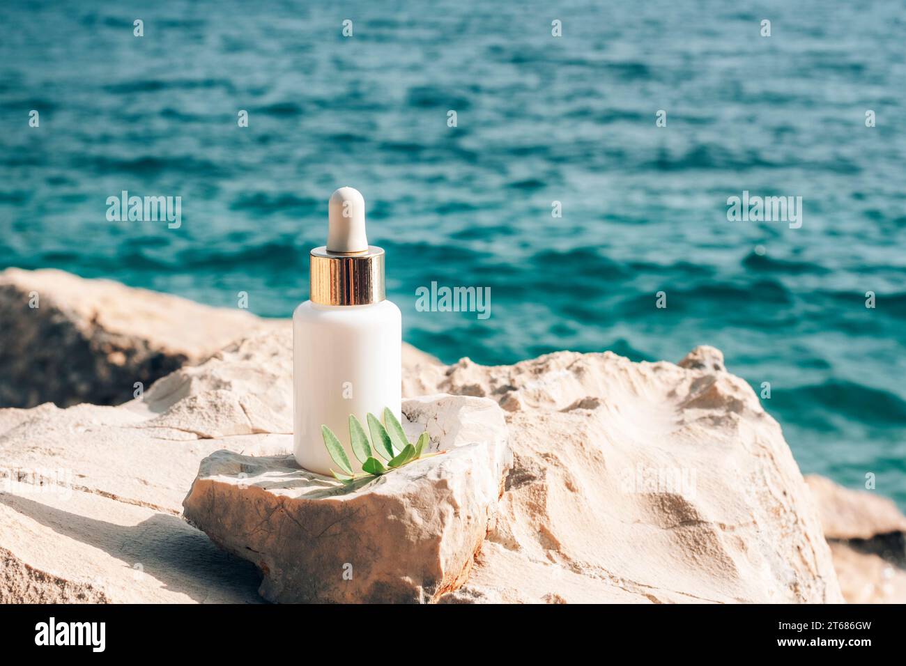 Kosmetische Serumflasche auf Stein auf dem Hintergrund des blauen Meeres, Nahaufnahme. Stockfoto