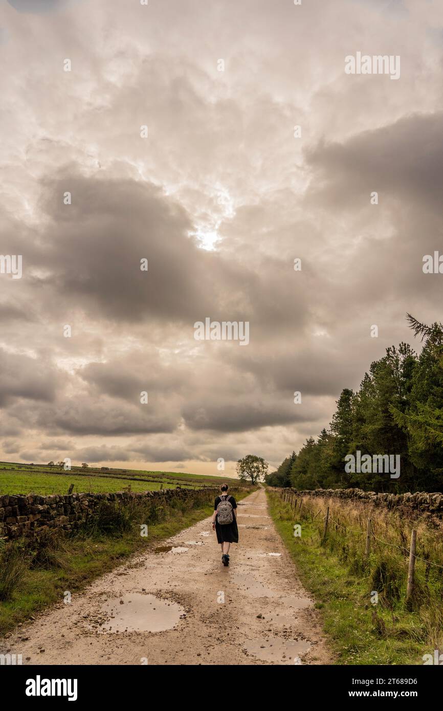 Mädchen in Kleid und Rucksack, das vor der Kamera auf einem schlammigen, nassen Pfad in Osmotherly, North Yorkshire, England, Großbritannien, unterwegs ist Stockfoto
