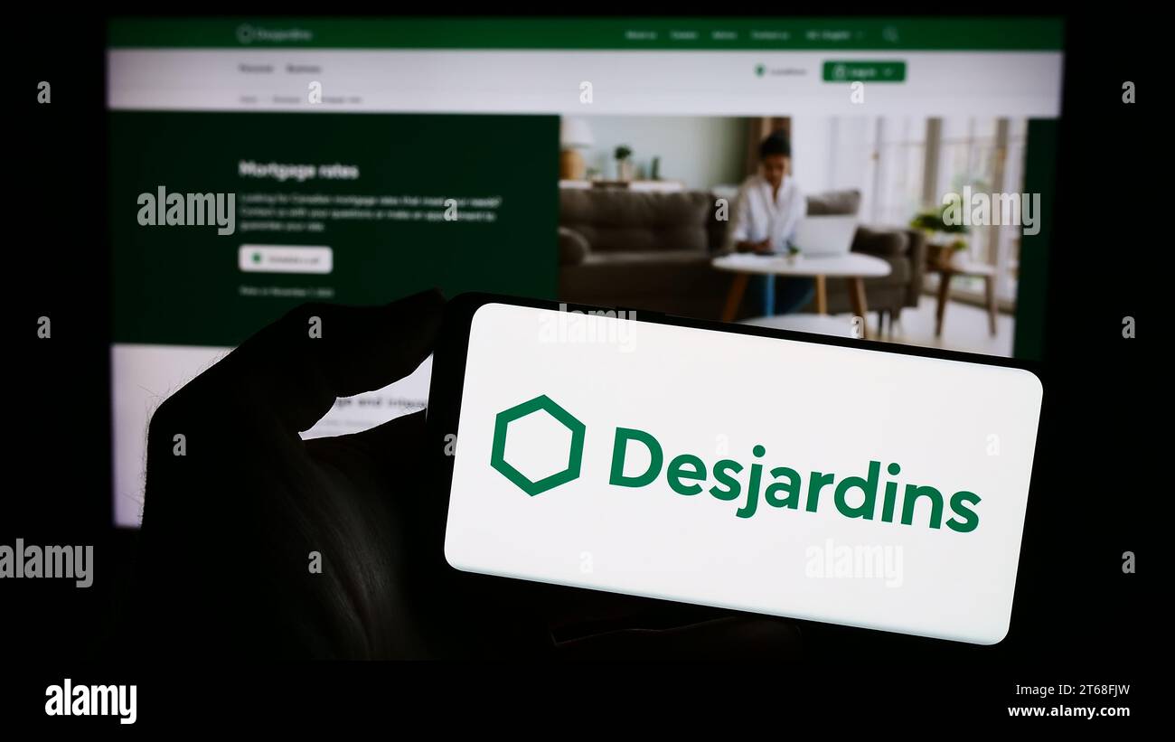 Person mit Mobiltelefon und Logo des kanadischen Finanzdienstleisters Desjardins Group vor der Webseite. Schwerpunkt auf dem Display des Telefons. Stockfoto