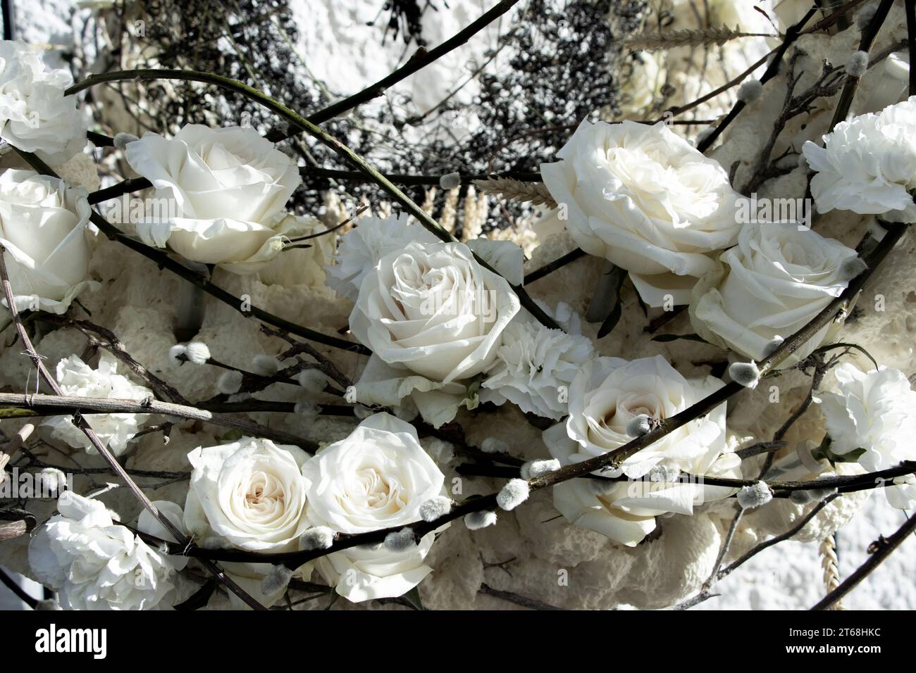 Teilbetrachtung eines Blumenarrangements aus weißen Rosen, Nelken und Weidenstäbchen mit Knospen. Blumenkunst. Stockfoto