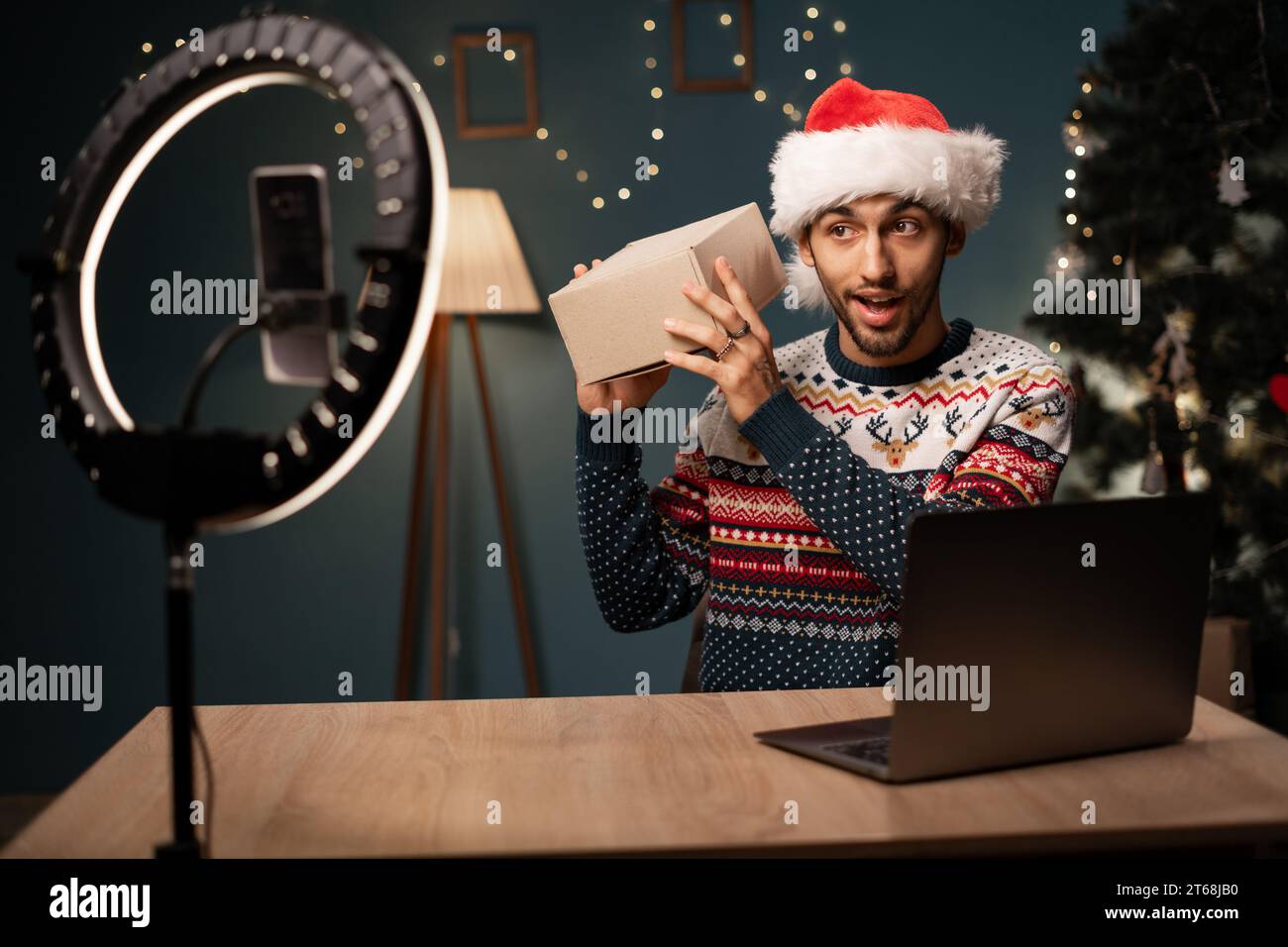 Glücklicher arabischer männlicher Blogger, der Geschenkboxen von Firmen auspackt und Livestreaming macht. Influencer mit Smartphone-Kamera zum Erstellen von Inhalten Stockfoto