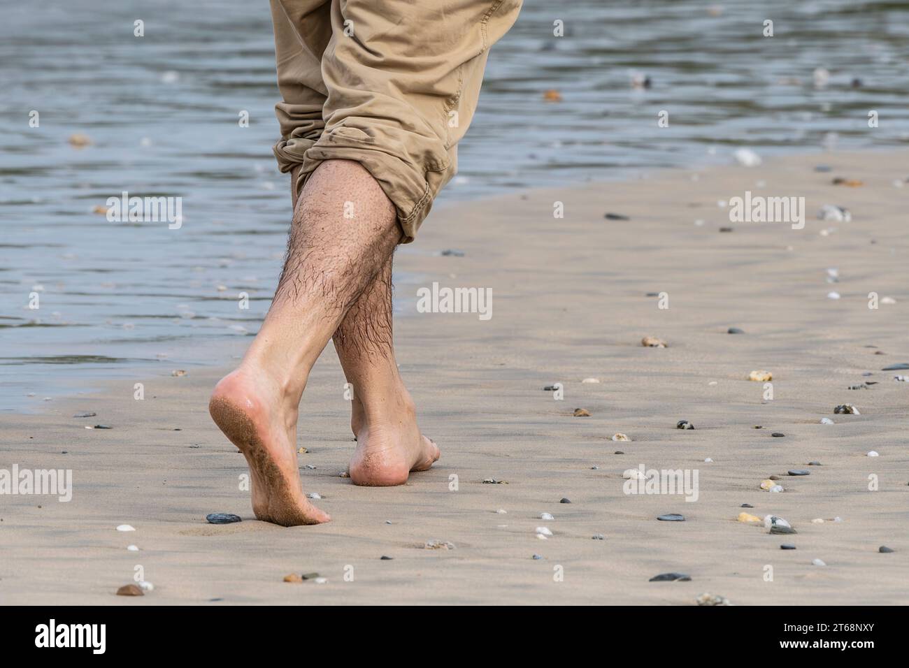 Ein Mann mit hochgerollten Hosen, der barfuß an der Küste am Fistral Beach in Newquay in Cornwall in Großbritannien läuft. Stockfoto