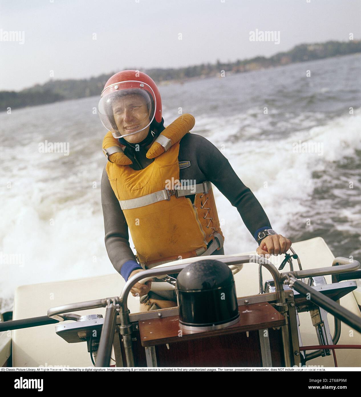 In den 1960er Jahren Ein Mann, der ein Motorboot fährt, gekleidet in einem Taucheranzug, einer Rettungsweste, einem Helm und einem Augenschutzglas. Er hat eine Hand am Lenkrad, eine am Gas. Schweden 1968. Kristoffersson Ref. DV13 Stockfoto