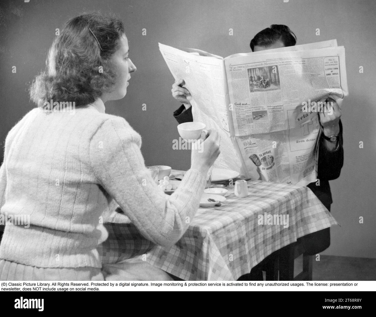 In den 1940er Jahren Ein Paar frühstückt und er hat sich in der heutigen Zeitung verloren. Schweden 1946 Stockfoto