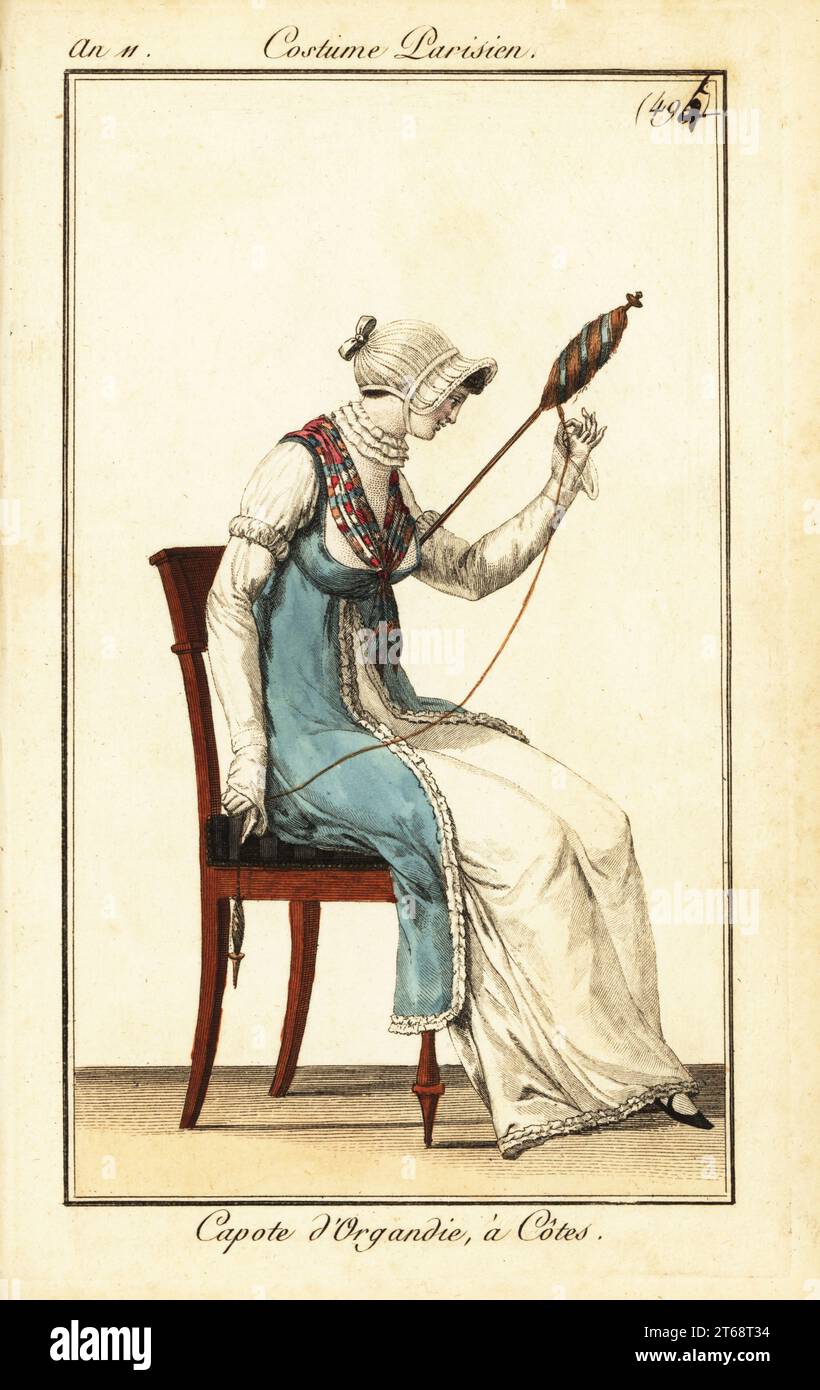 Frau, die Garn mit Spindel und Distau spinnt, Paris, 1803. Sie trägt eine Kapuzenmütze in gerippter Organdy, blaue Tunika über einem weißen Kleid, Rüschenkragen und Fichu. Capote dOrgandie, à Côtes. Handkolorierter Kupferstich aus Pierre de la Mesangeres Journal des Dames et des Modes, Zeitschrift für Frauen und Mode, Paris, an 11, 1803. Illustrationen von Carle Vernet, Jean-Francois Bosio, Dominique Bosio und Philibert Louis Debucourt, Kupferstich von Pierre-Charles Baquoy. Stockfoto