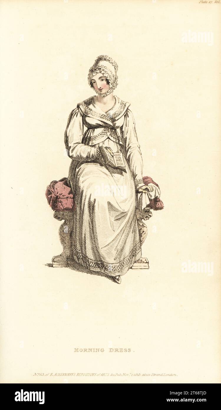 Regency Frau im Morgenkleid und Mob Mütze lesen ein Buch. In französischer Jacke und Petticoat aus kambrischem Musselin, französischer Mob-Mütze aus Satin und gequillter Spitze. Vol. 14, Platte 27, 1. November 1815. Handkolorierter Kupferstich von Thomas Uwins aus Rudolph Ackermanns Repository of Arts, Strand, London. Stockfoto