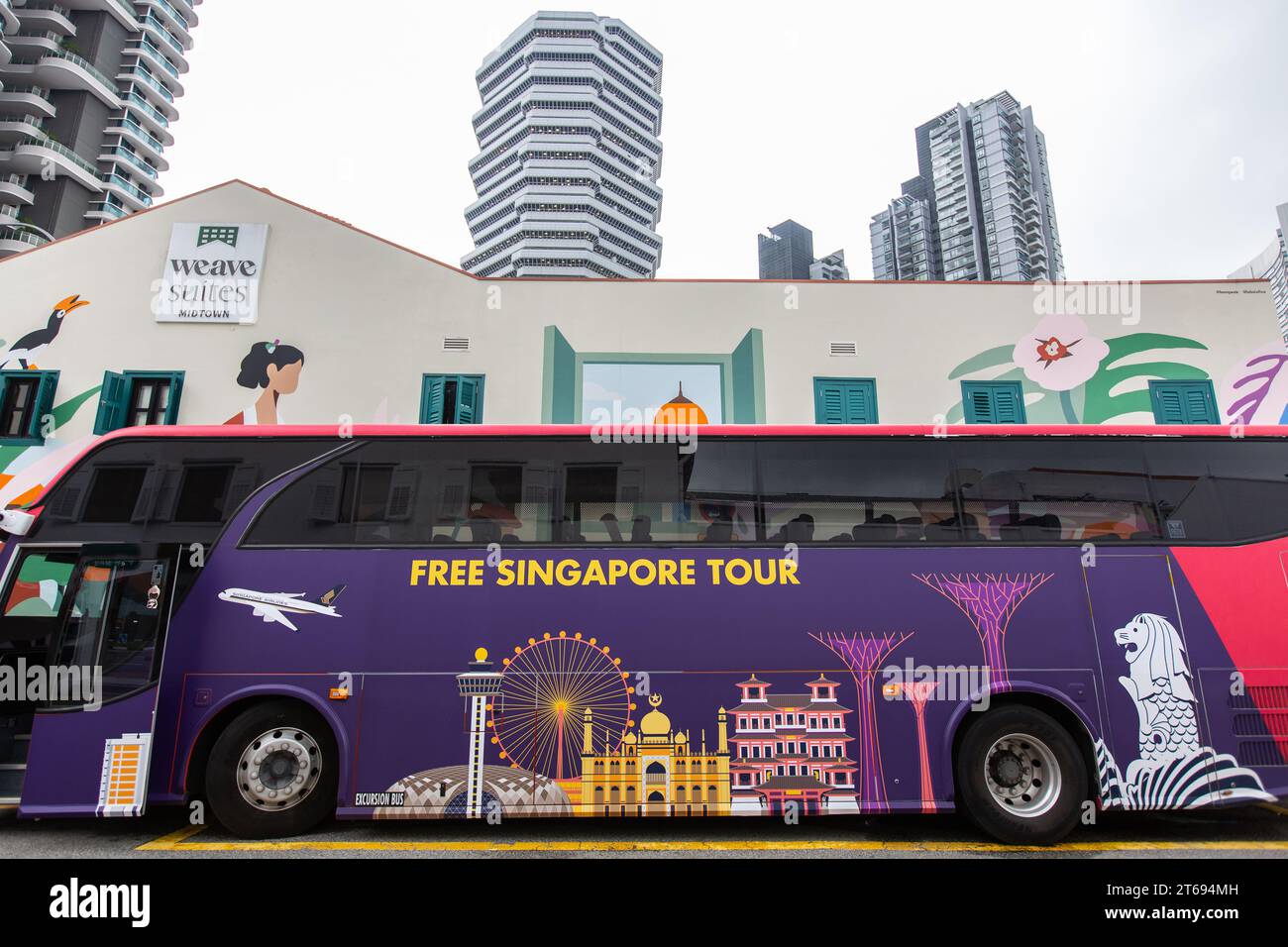 Ein Bus mit den Worten Free Singapore Tour, Wahrzeichen Grafiken, Park entlang der Straße, Tageszeit, keine Leute, Singapur. Stockfoto