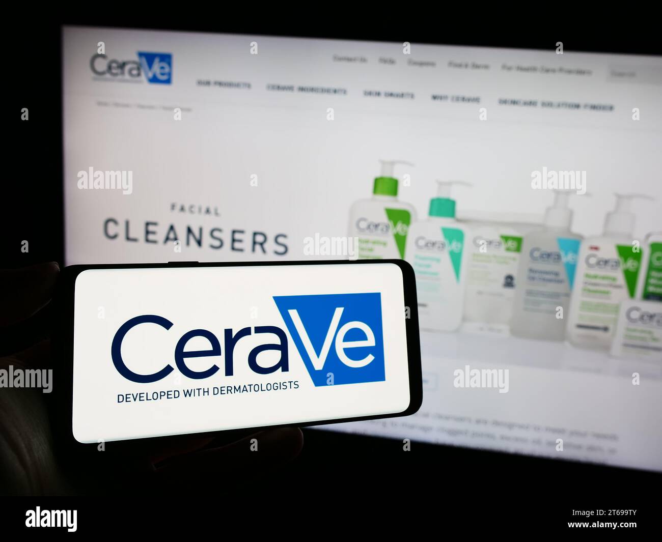 Person, die ein Mobiltelefon mit dem Logo des Körperpflegeunternehmens CeraVe (L’Oreal) vor der Webseite hält. Schwerpunkt auf dem Display des Telefons. Stockfoto