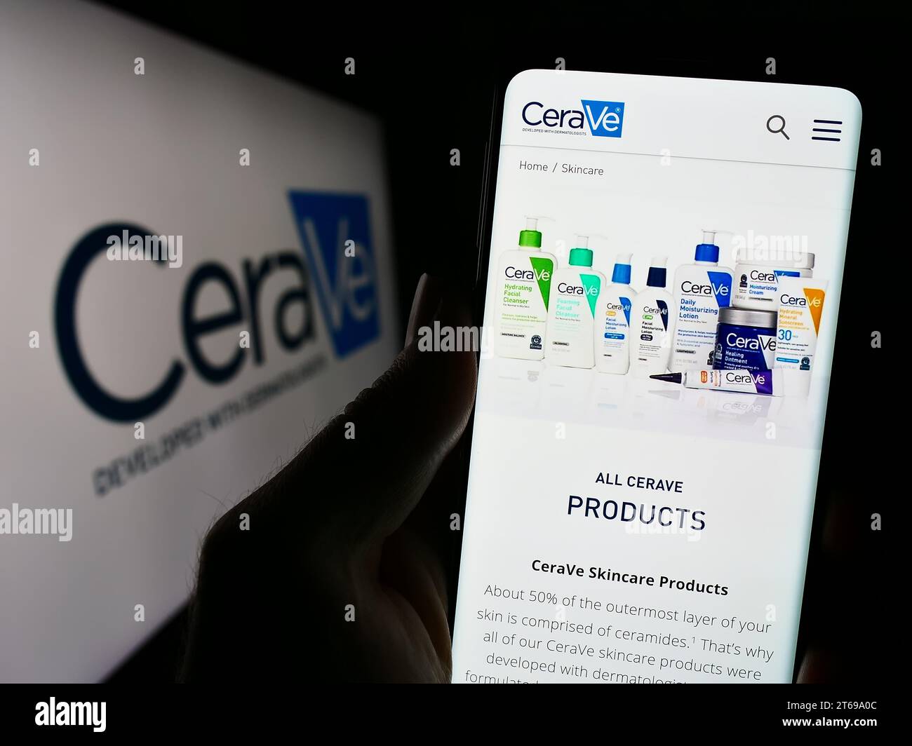 Person mit Smartphone und Website des Körperpflegeunternehmens CeraVe (L’Oreal) vor dem Firmenlogo. Konzentrieren Sie sich auf die Mitte des Telefondisplays. Stockfoto