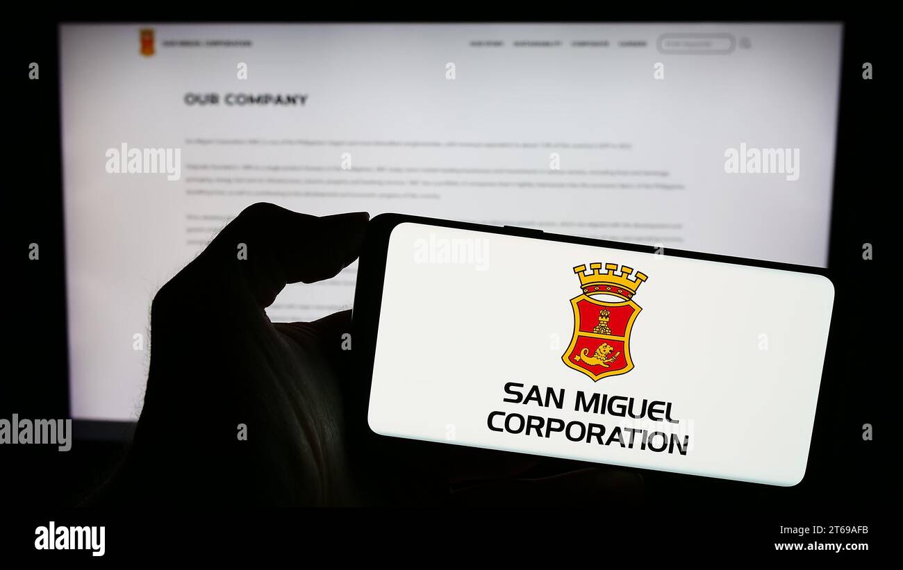 Person mit Smartphone und Logo der philippinischen Firma San Miguel Corporation (SMC) vor der Website. Schwerpunkt auf dem Display des Telefons. Stockfoto