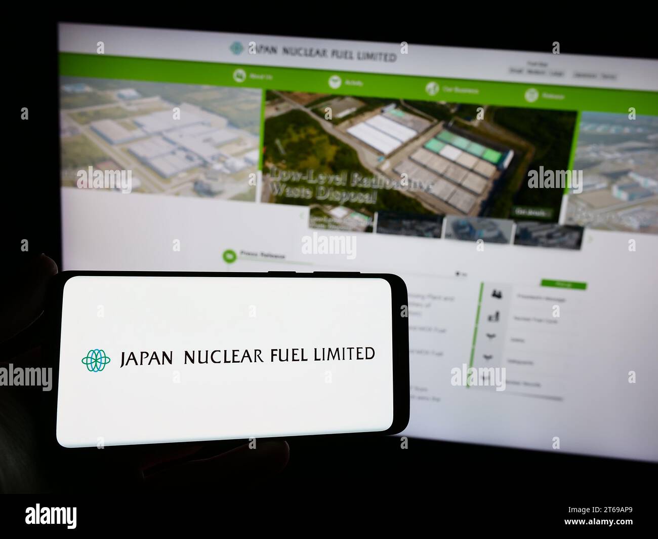 Person mit Smartphone und Logo des japanischen Energieunternehmens Japan Nuclear Fuel Ltd (JNFL) vor der Website. Schwerpunkt auf dem Display des Telefons. Stockfoto